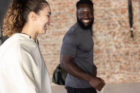 Laughing diverse friends walking in urban fitness studio with brick wall background