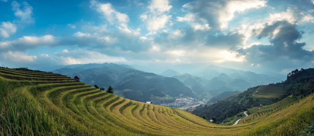 Panoramic view of terraced rice fields in a mountainous landscape, showcasing lush green terraces and a dramatic sky. Ideal for use in travel brochures, environmental posters, and agricultural articles. Perfect for themes focused on nature, rural life, sustainable farming, or scenic photography.