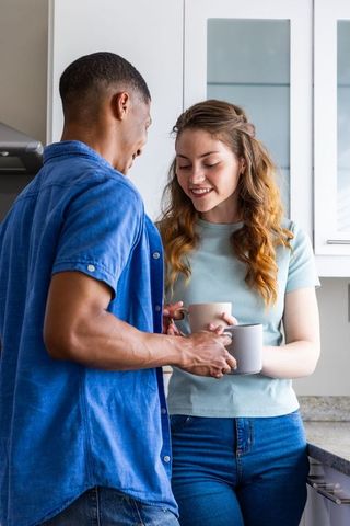 Multiracial couple sharing morning coffee and smiling at bright modern kitchen counter
