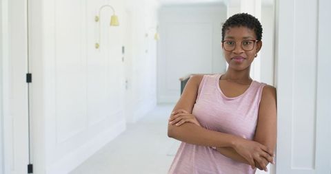 African american woman leaning in bright white hallway wearing pink top and glasses