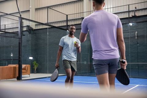 Diverse male players playing padel on indoor blue court practicing rally