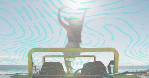 Backlit woman raising arms on yellow dune buggy at sunny beach with turquoise overlay
