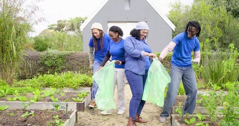 Diverse volunteers gardening together in community garden holding green bags and tools