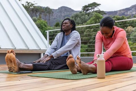 African american couple stretching together on rooftop yoga mats with mountain view