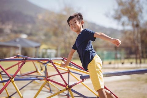 Asian Boy Balancing on Colorful Climbing Dome in Sunny Playground