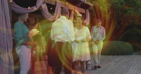 Intimate outdoor wedding vows under draped pergola at twilight with romantic lens flare