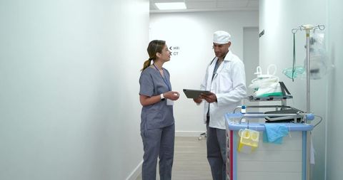 African american doctor and nurse reviewing tablet in hospital corridor near radiology