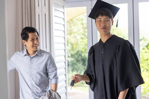Asian graduate son receiving car keys from proud father at home doorway