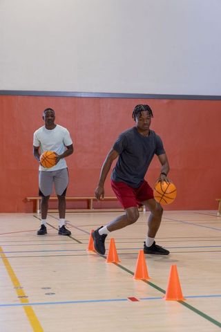 African american men practicing basketball dribbling drills through cones on gym court