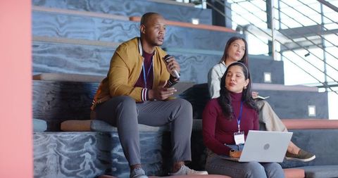Diverse team collaborating on tiered steps, man with microphone, woman with laptop