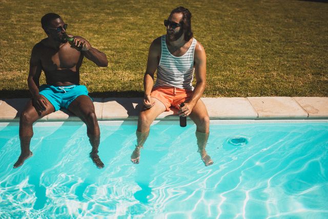 Two diverse male friends sitting by the pool, enjoying beers and chatting on a sunny summer day. Perfect for illustrating themes of friendship, leisure, outdoor activities, and summer fun. Ideal for use in advertisements, social media posts, and lifestyle blogs.