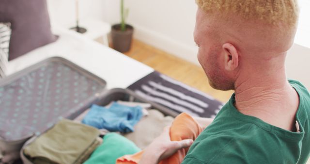 Image depicts a man packing a suitcase in a bedroom, organizing clothes for a trip. Ideal for use in lifestyle articles about travel preparation, vacation planning, and time management tips. Could also be used in advertisements for travel gear, luggage, and vacation promotions.