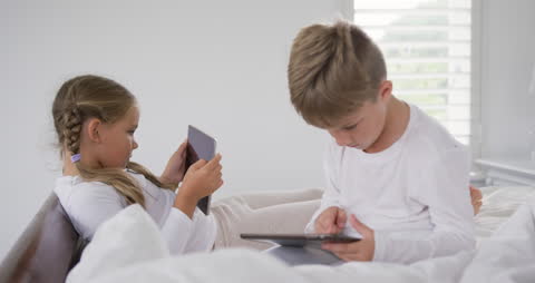 Siblings Using Tablets on Bed for Home Entertainment