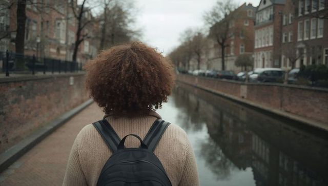 Woman walking along canal with backpack on overcast autumn day urban reflection