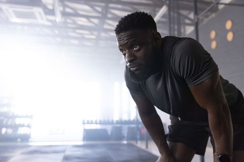 Muscular african american man resting after workout leaning on knees in industrial gym