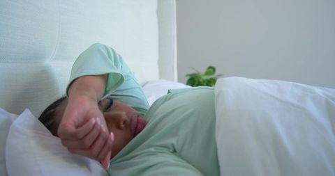Relaxing african american woman resting in bed with mint green top in minimalist bedroom