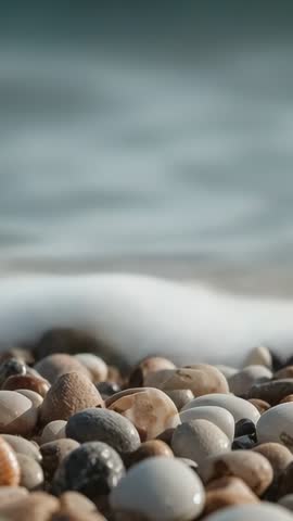 Vertical video: Swell lapping multicolored pebbles with receding foam and wet stones