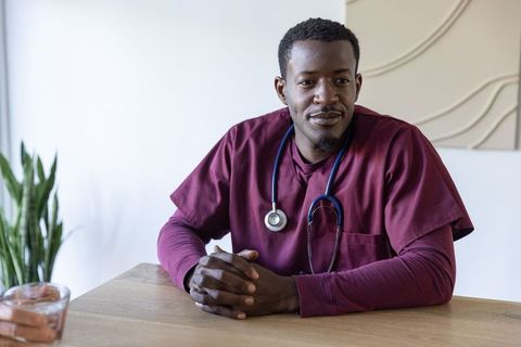 African american clinician sitting at table wearing maroon scrubs and stethoscope