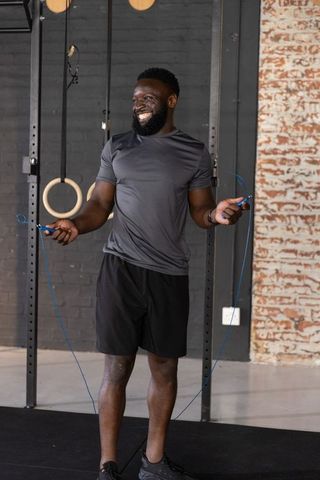 Smiling african american man skipping rope in industrial gym with gymnastic rings