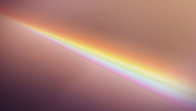 Diagonal prismatic streak on macro lens surface, pastel halo and soft rainbow gradient
