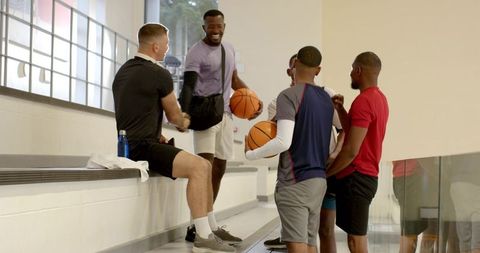 Diverse male friends greeting and grabbing basketballs before pickup game in indoor court