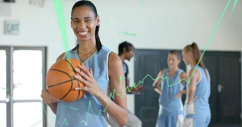 Smiling basketball player holding basketball with teammates practicing on indoor gym court