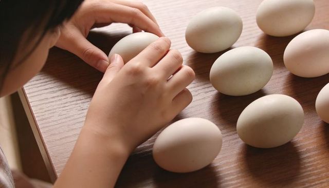 Child arranging pale eggs on wooden table closeup hands sorting organic eggs