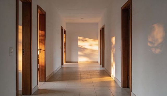Sunlight casting warm shadows along minimalist corridor with open wooden doorways