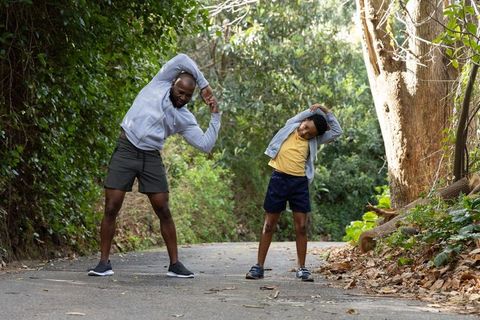 Father and son stretching together on woodland trail during outdoor family fitness routine