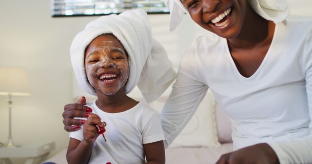 Happy african american mother and daughter wearing towels sitting on bed and looking to camera. staying at home in self isolation during quarantine lockdown.