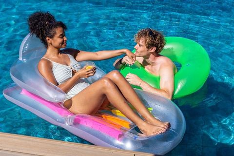 Couple enjoying sunny pool float: woman relaxing on clear lounger while man kissing hand