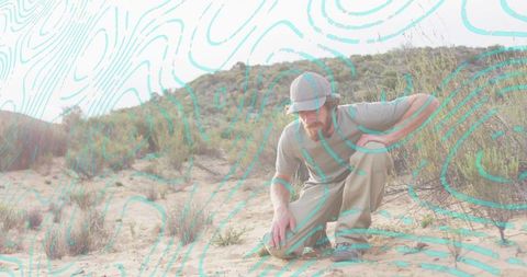 Kneeling hiker inspecting coastal dune with turquoise topographic overlay