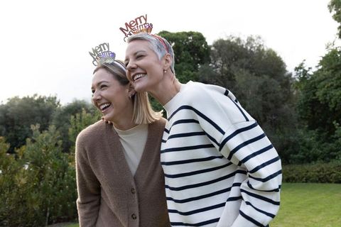Two women laughing in garden wearing merry christmas headbands celebrating holiday joy