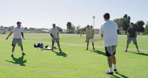 Multiethnic men playing casual cricket on sunny park field practicing teamwork and fitness