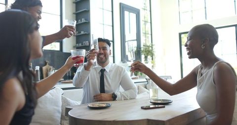 Friends raising glasses around dining table in modern bright open-plan kitchen
