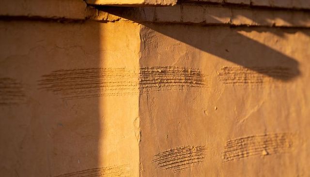 Sunlight casting diagonal shadow on ochre stucco corner with trowel groove texture