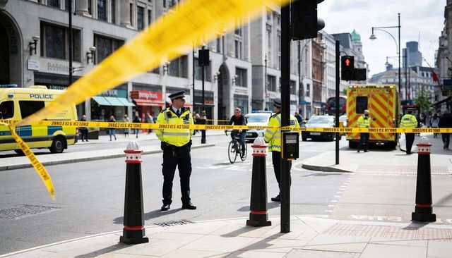 Police cordon securing urban street with ambulance response and emergency crews on scene