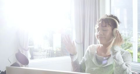 Mid-adult african american woman listening and adjusting headphones in sunlit home office
