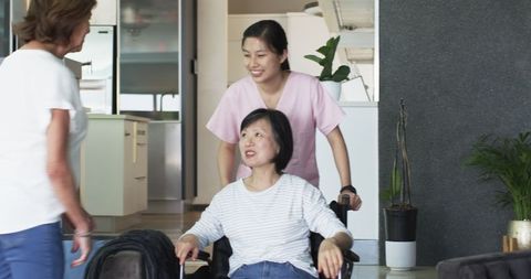 Senior Woman in Wheelchair with Caring Nurse and Friend in Living Room