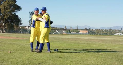 Teammates Celebrating Baseball Win Embracing on Sunny Field in Yellow and Blue Uniforms