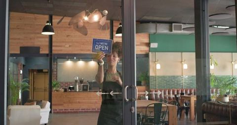 Barista hanging open sign on glass door of cafe with industrial wood interior