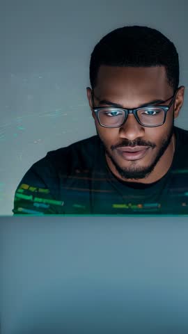 Black man leaning into laptop reading code with green glow, vertical coding video