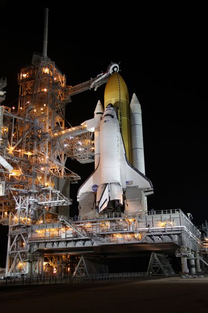NASA's space shuttle Discovery is positioned on Launch Pad 39A at Kennedy Space Center in Florida at night. The rotating service structure has been rolled back, revealing the shuttle and its attached external fuel tank. The setup benefits from advanced technology like the oxygen vent hood, which vents vapors away from the shuttle. This specific mission, STS-128, will involve a 13-day journey to the International Space Station to deliver new equipment, a freezer for samples, and more. The image is perfect for content related to space exploration, aerospace technology, and NASA's historic missions.