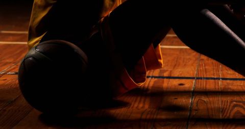 Athlete resting with basketball on court floor in low light