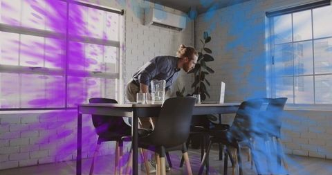 Man with bun leaning over laptop at conference table in modern minimalist loft workspace
