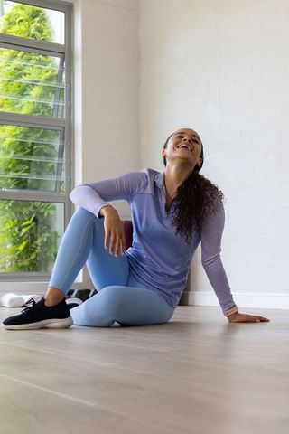 Smiling african american woman relaxing after workout by window in lilac activewear