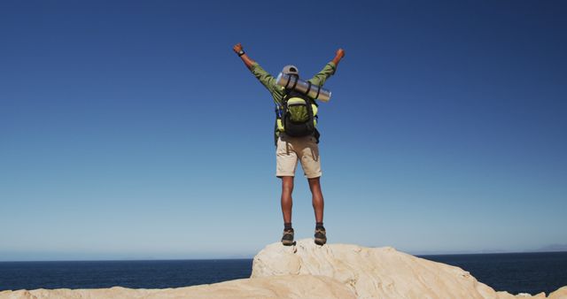 African american man hiking in mountains standing on rock raising his hands by the sea. fitness training and healthy outdoor lifestyle.