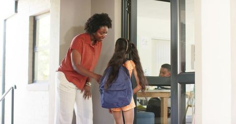African american teacher welcoming young student with backpack into classroom
