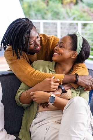 African american couple embracing on sofa, smiling and laughing, cozy romance at home balcony