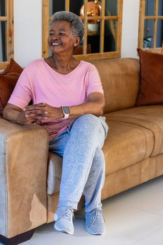 Senior african woman sitting on tan leather sofa wearing smartwatch and smiling